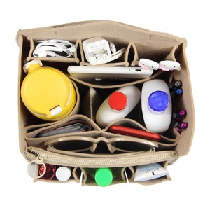 Op de afbeelding: Een beige feltaschenorganizer met meerdere vakken. De organizer is gevuld met verschillende items, waaronder een waterfles, een telefoon, een zonnebril, een oplader en toiletartikelen.
