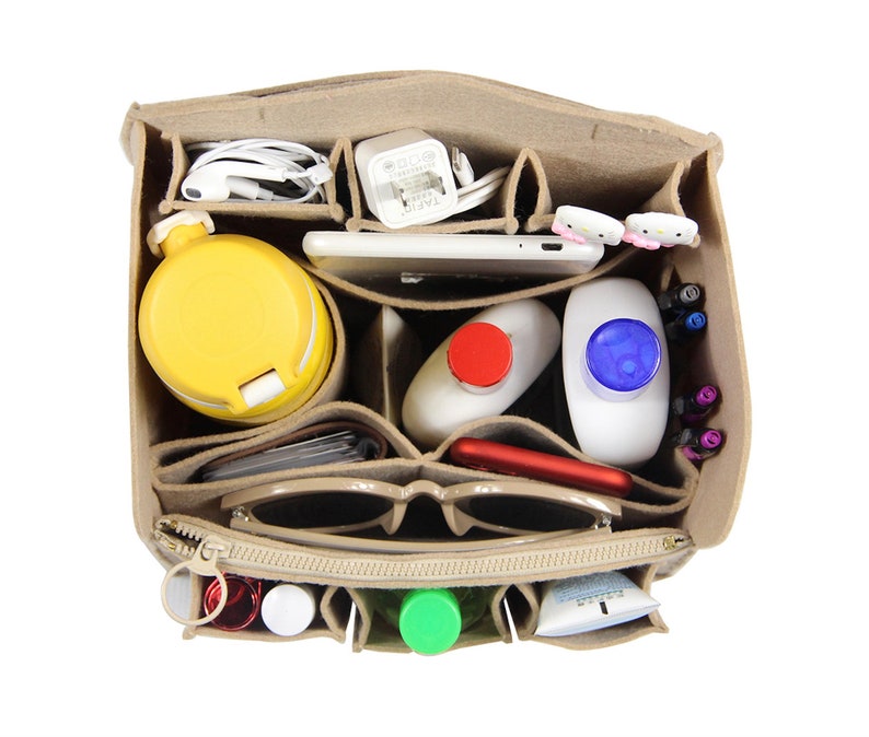 Op de afbeelding: Een beige feltaschenorganizer met meerdere vakken. De organizer is gevuld met verschillende items, waaronder een waterfles, een telefoon, een zonnebril, een oplader en toiletartikelen.