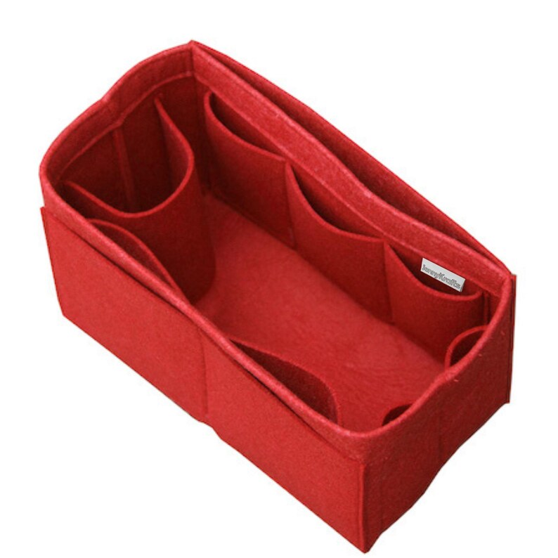May include: A rectangular red felt handbag organizer insert featuring multiple interior compartments and pockets of varying sizes to help keep items organized. A small white rectangular tag is attached to the inner side wall of the felt structure.