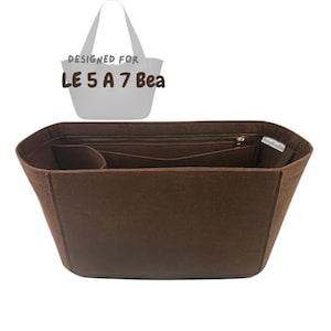 Puede incluir: Organizador de bolso de mano de fieltro marrón con múltiples compartimentos y un bolsillo con cremallera. El organizador está diseñado para adaptarse a un modelo de bolso específico, con el texto "DESIGNED FOR LE 5 A 7 Bea" visible. Forma rectangular.