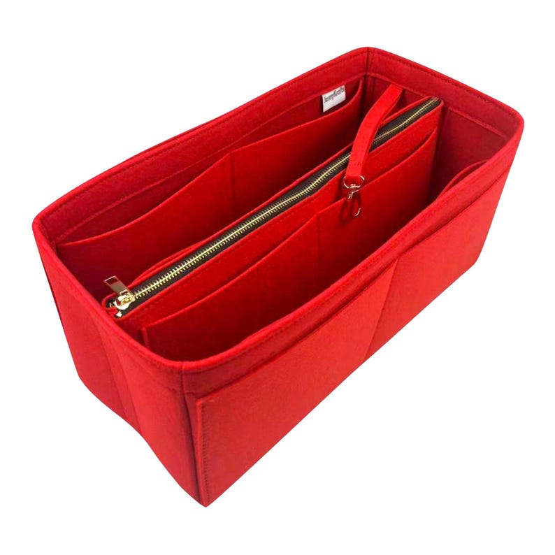May include: A vibrant red felt handbag organiser with multiple compartments and a zipped section. The organiser has a gold-coloured zip and a small handle. The interior is divided into several pockets for storage.