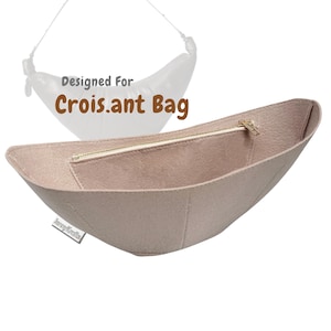 May include: A beige felt bag organizer with a gold zipper, designed for a Crois.ant Bag. The organizer has a curved shape and a small pocket inside. The text "Designed For Crois.ant Bag" is visible in the background.