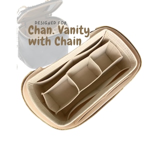 Puede incluir: Organizador interior beige con múltiples compartimentos para un neceser. El organizador tiene cierre de cremallera y está diseñado para un tipo específico de neceser. El texto "DESIGNED FOR Chan. Vanity with Chain" es visible.