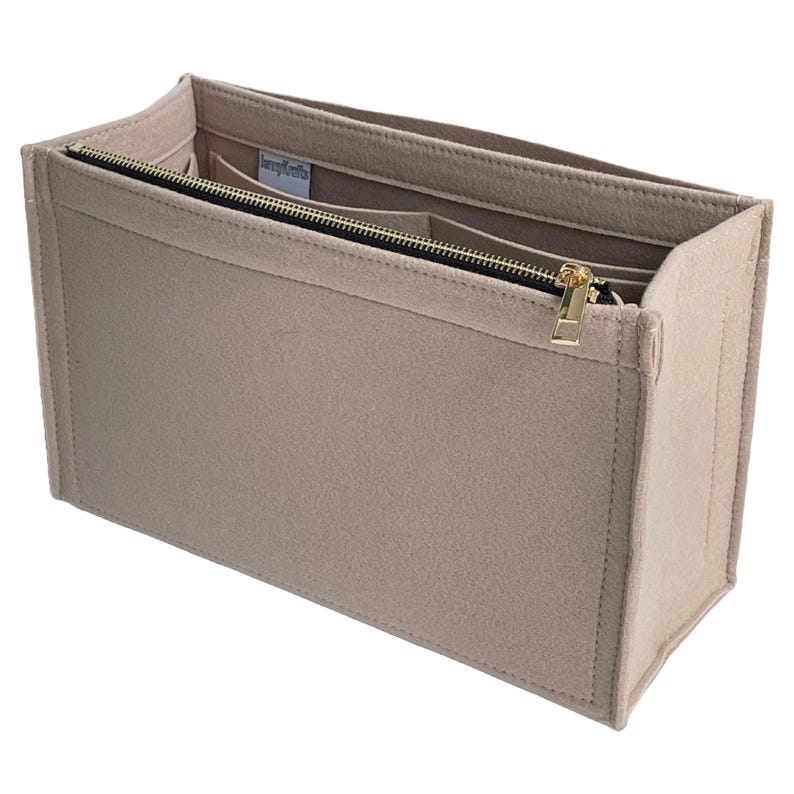 Op de afbeelding: Beige vilten handtassenorganizer met een goudkleurige rits en meerdere binnenvakken. De organizer is rechthoekig en ontworpen om in een grotere tas te passen, voor structuur en organisatie. De rits loopt over de bovenkant.