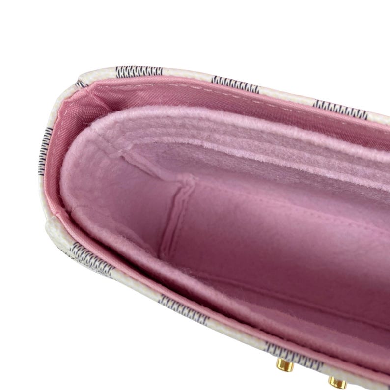 Op de afbeelding: Close-up van een handtas organizer met een roze binnenkant en een witte buitenkant met zwarte rand. De organizer heeft meerdere compartimenten en is ontworpen om items georganiseerd te houden. Goudkleurige hardware is zichtbaar aan de onderkant.