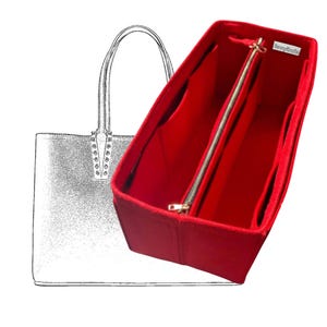 May include: A bright red handbag organizer with multiple compartments and a zippered center section. The organizer is designed to fit inside a tote bag, as shown in the sketch of a tote bag in the background. The organizer has a gold-colored zipper.