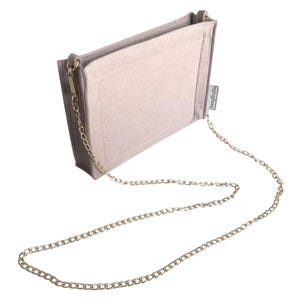 May include: A light grey handbag organiser with a gold-coloured chain strap. The organiser is rectangular with a soft, felt-like texture and a small tag on the side. The chain is attached to the bag with gold-coloured clasps.