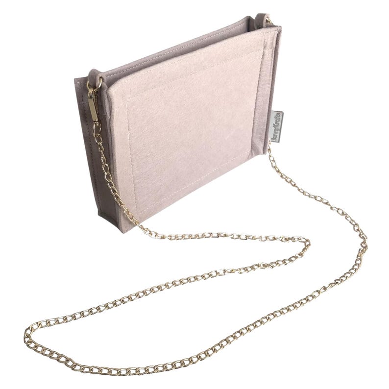 May include: A light grey handbag organiser with a gold-coloured chain strap. The organiser is rectangular with a soft, felt-like texture and a small tag on the side. The chain is attached to the bag with gold-coloured clasps.