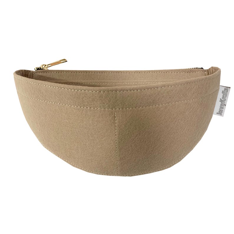 May include: A beige felt handbag organizer with a curved shape and a gold-colored zipper. The organizer has a stitched design and a small white tag that reads "JennyKrafts". The bag is designed to help organize the contents of a handbag.