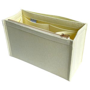 Op de afbeelding: Een cr&egrave;mekleurige vilten tassenorganizer met een gouden rits en meerdere binnenvakken. De organizer is rechthoekig en ontworpen om in een grotere tas te passen, voor structuur en organisatie. De binnenkant is lichtcr&egrave;me.