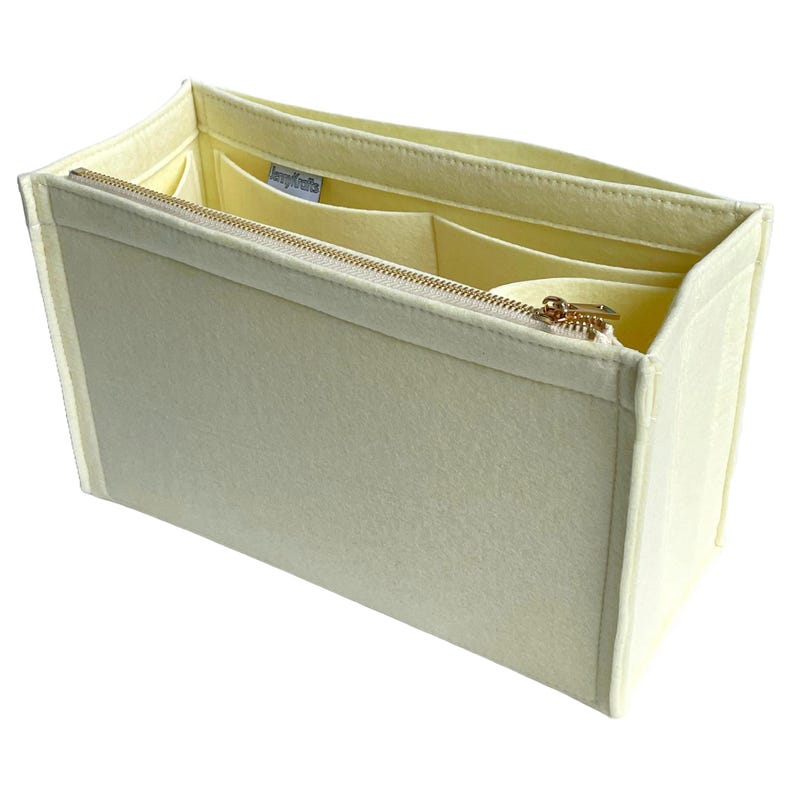 Op de afbeelding: Een cr&egrave;mekleurige vilten tassenorganizer met een gouden rits en meerdere binnenvakken. De organizer is rechthoekig en ontworpen om in een grotere tas te passen, voor structuur en organisatie. De binnenkant is lichtcr&egrave;me.