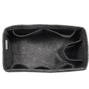 May include: A dark gray felt bag organizer with a rectangular shape, featuring multiple interior compartments and pockets for storage. A small white fabric tag with black text is attached to the inner side wall of the felt organizer.