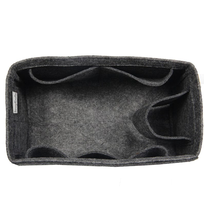 May include: A dark gray felt bag organizer with a rectangular shape, featuring multiple interior compartments and pockets for storage. A small white fabric tag with black text is attached to the inner side wall of the felt organizer.