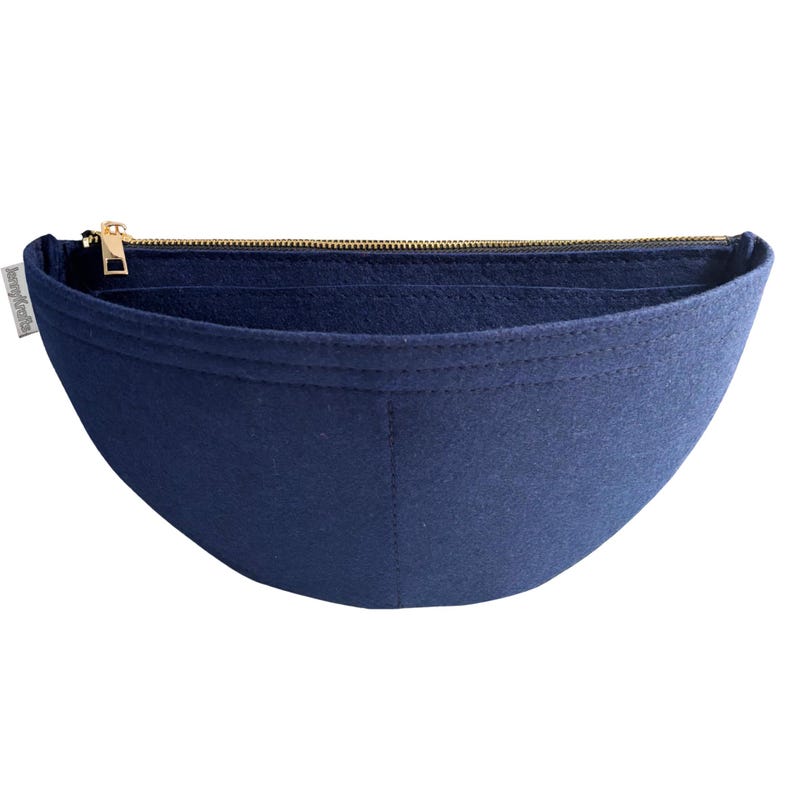 May include: A navy blue felt bag organizer with a gold zipper closure. The organizer has a curved shape and is designed to fit inside a handbag. A small white tag with text is visible on the side.