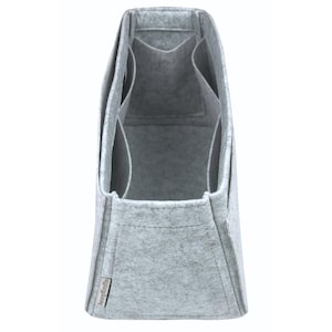 May include: A grey felt bag organiser with multiple compartments. The organiser has a rectangular shape with a structured design. It features several pockets and dividers for storage. The material appears to be a soft, felt-like fabric.
