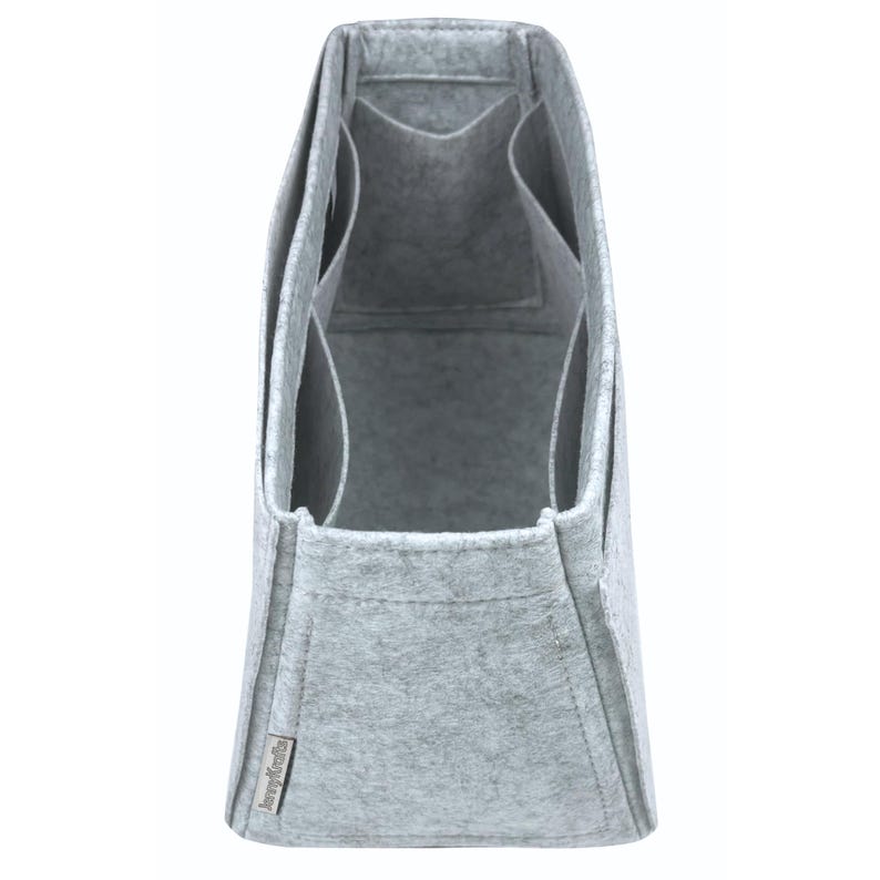 May include: A grey felt bag organiser with multiple compartments. The organiser has a rectangular shape with a structured design. It features several pockets and dividers for storage. The material appears to be a soft, felt-like fabric.