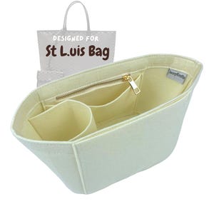 Puede incluir: Un organizador de bolso de fieltro color crema con varios bolsillos y un compartimento con cremallera. El organizador está diseñado para el bolso St. Louis. El texto "Designed for St. Louis Bag" es visible en la parte superior del organizador.