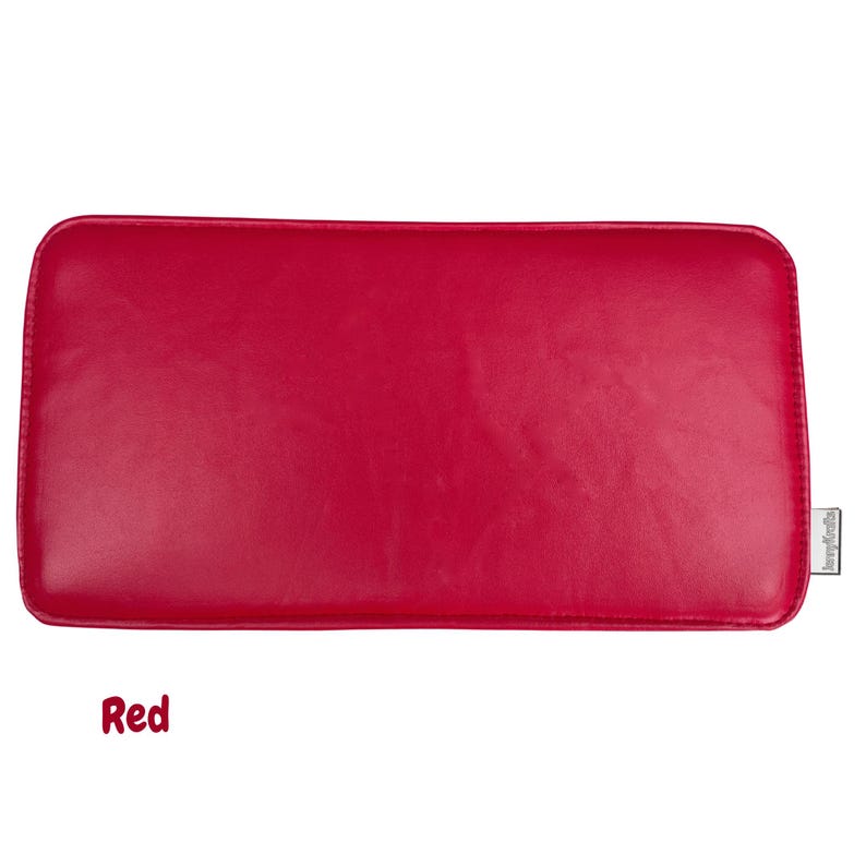 May include: A rectangular, red leather cushion with rounded corners. The word "Red" is written in a cursive font at the bottom left. A small tag with text is on the right side.