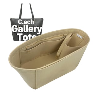 May include: Beige felt tote bag organizer with multiple compartments and a zippered pocket. The organizer has a gold zipper and a small strap with a gold clasp. A black tote bag with the text "C.ach Gallery Tote" is in the background.