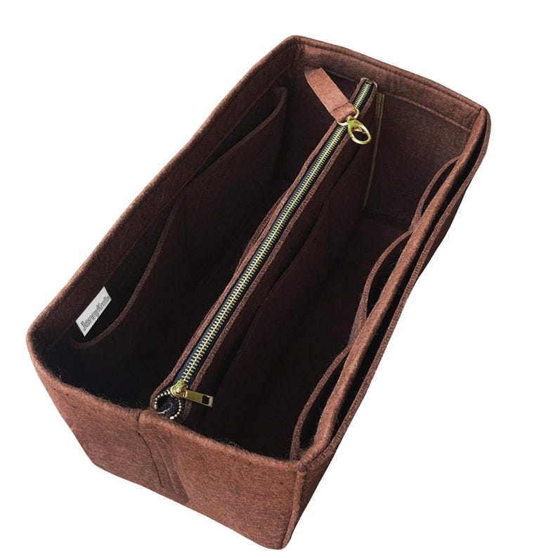 May include: A brown felt handbag organiser with multiple compartments and a zipped central section. The organiser has a rectangular shape and a light brown zip with a gold-coloured pull. The brand name is visible on a small white tag.