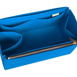 Può includere: Un organizzatore per borsa in feltro blu con più tasche e una chiusura a zip. L'organizzatore ha una piccola etichetta verde che dice "Felt Goods".