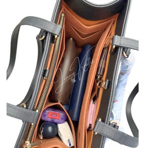 May include: A grey tote bag with an internal organiser. The interior has multiple compartments and pockets in shades of brown and orange, with various items stored inside. The bag has two handles and a zip closure.
