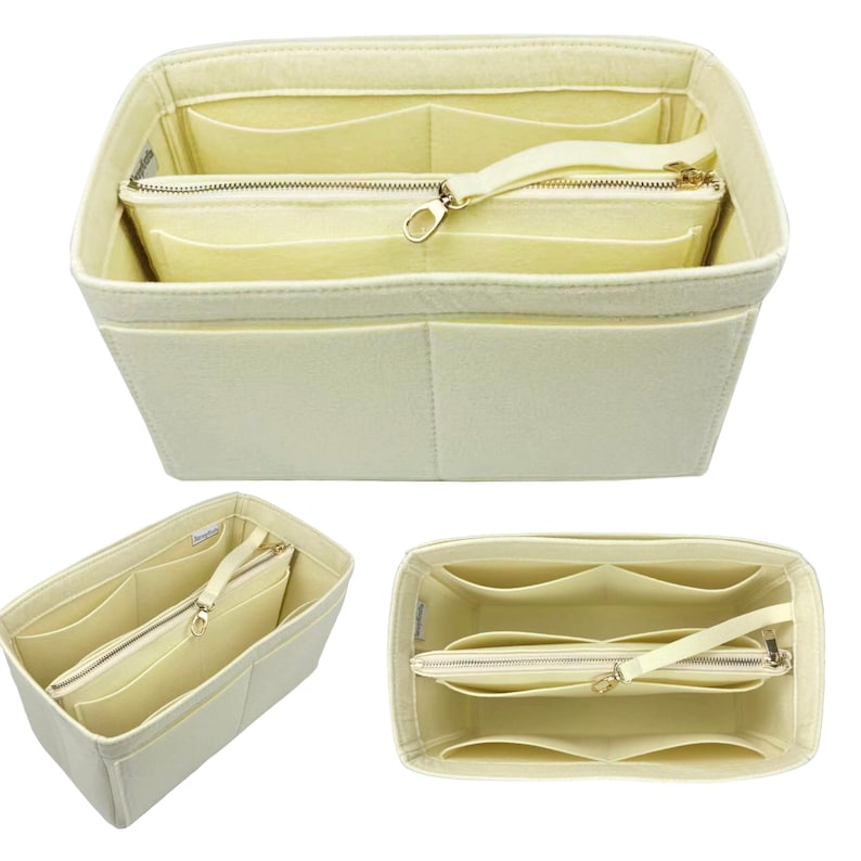 May include: Cream-coloured felt handbag organiser with multiple compartments and a zipped pouch. The organiser has a rectangular shape with a structured design, featuring a handle and a gold-toned zip.