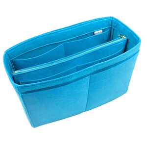 May include: A turquoise felt handbag organiser with multiple compartments and a zipped section. The organiser has a rectangular shape and is designed to fit inside a larger bag, providing structure and organisation.