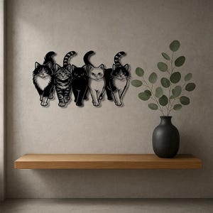 May include: A metal wall art piece featuring five stylized cat silhouettes. The cats are in various colors, including black, white, and tabby patterns. The artwork is mounted on a neutral-colored wall above a wooden shelf.