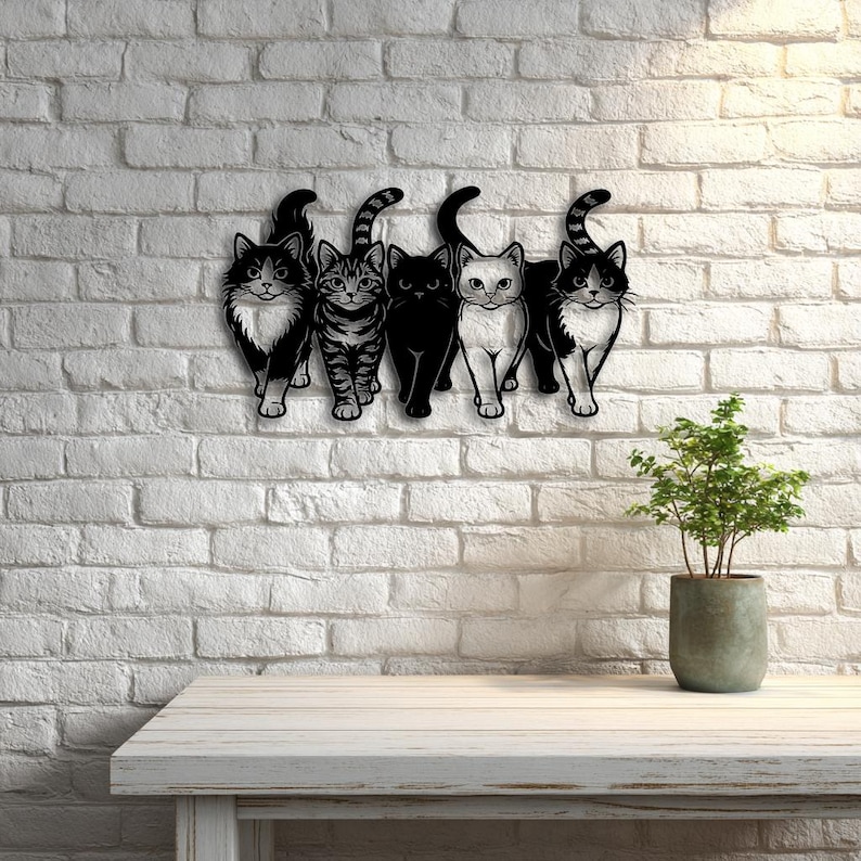May include: A black metal wall art piece featuring five stylized cat silhouettes. Each cat has a unique pattern, including solid black, tabby stripes, and tuxedo markings. The cats are mounted on a white brick wall.