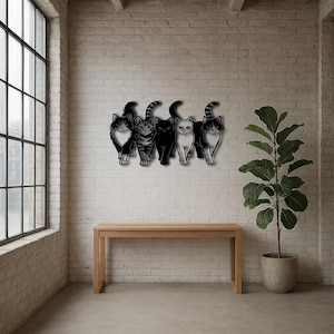 May include: A wall-mounted metal art piece featuring five stylized cat silhouettes. The cats are in various poses, with different patterns and colors, including black, white, and tabby. The artwork is mounted on a white brick wall above a wooden table.