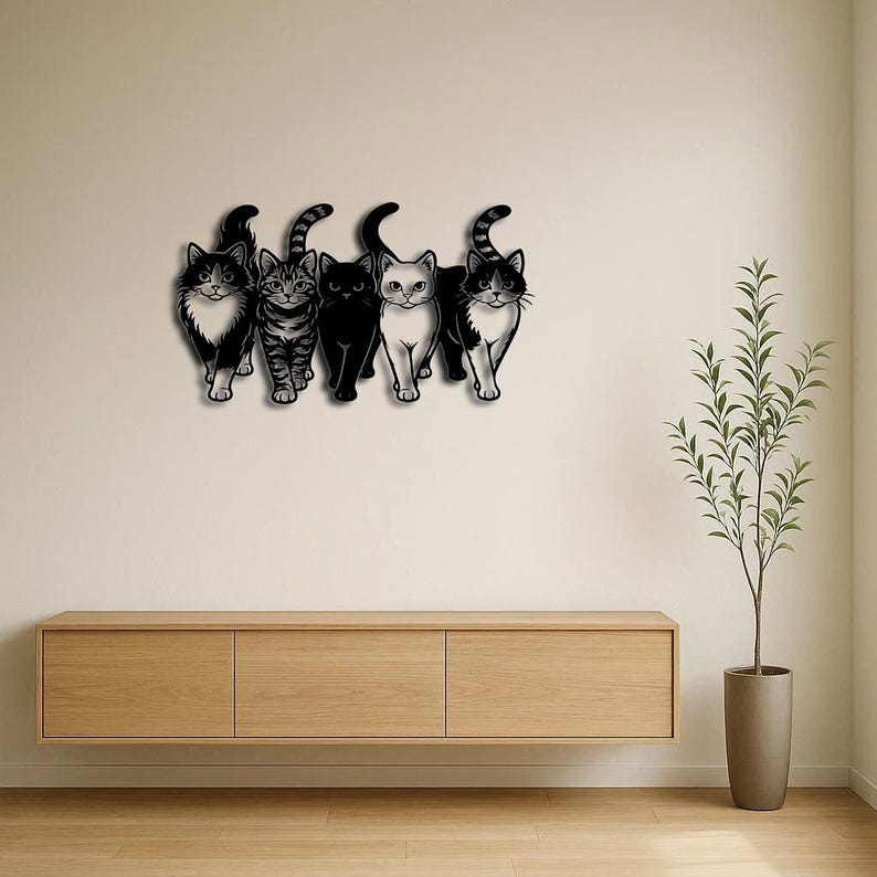 May include: A black metal wall art piece featuring five stylized cats in a row. Each cat has a unique pattern, including solid black, tabby stripes, and tuxedo markings. The artwork is mounted on a neutral-colored wall above a wooden cabinet.