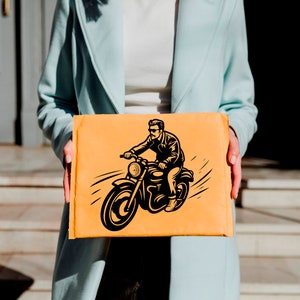 May include: An orange package featuring a black and white illustration of a person riding a motorcycle. The package is held by a person wearing a light blue coat.