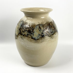 May include: A beige ceramic vase with a wide mouth and a rounded body. The vase has a brown and blue glaze with a mottled effect.