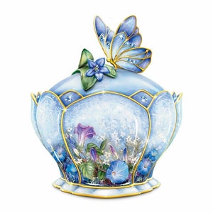 May include: A light blue decorative trinket box with a butterfly and floral design. The box features a butterfly on the lid, with blue and gold accents. The box has a floral design with blue and purple flowers.