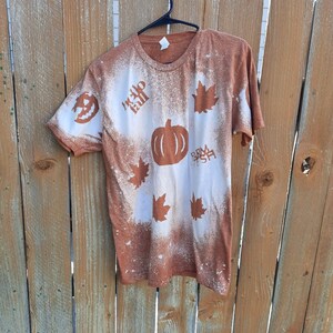 May include: A brown t-shirt with a bleach-splattered design featuring a pumpkin, maple leaves, and the text "Hello Fall" and "Farm Fresh".