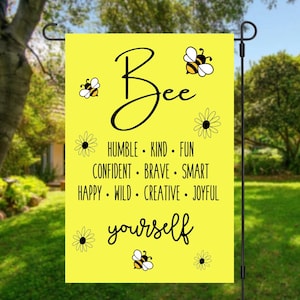 May include: Yellow garden flag with a bee illustration and the text "Bee yourself" with a list of positive adjectives below. The flag has a black border and white daisy illustrations.