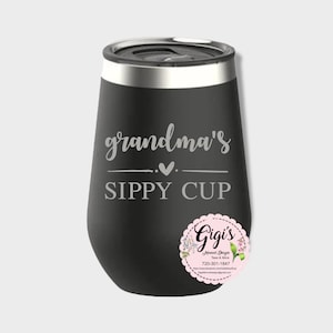 May include: A matte black stainless steel tumbler with a silver rim and lid. The front features the engraved text "grandma's" above a small heart and the words "SIPPY CUP" in capital letters. A circular pink logo sticker is attached.