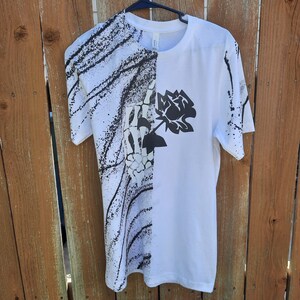 Peut inclure: T-shirt blanc avec un imprim&eacute; graphique noir et blanc d'une main squelettique tenant une rose. Le graphique est sur le c&ocirc;t&eacute; gauche du t-shirt, et le c&ocirc;t&eacute; droit est blanc uni.