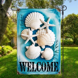 Puede incluir: Una bandera de jardín con un fondo azul con conchas marinas y estrellas de mar blancas. La palabra "WELCOME" está impresa en negro en la parte inferior. La bandera se exhibe al aire libre en un soporte de metal negro.