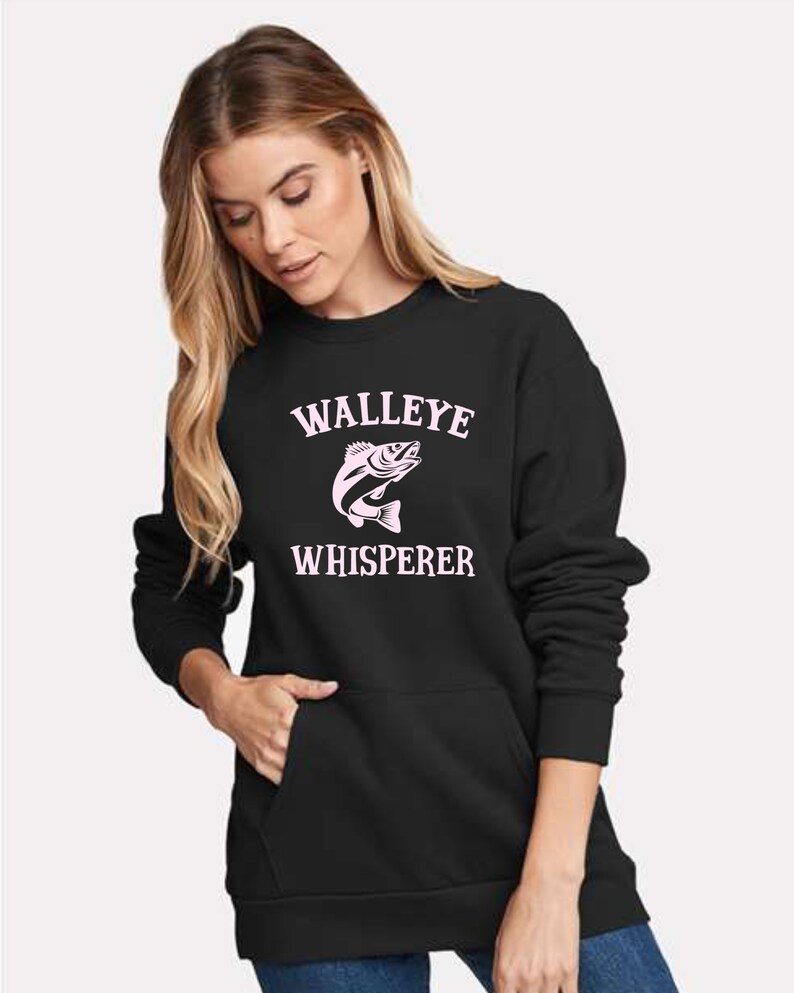 K&ouml;nnte beinhalten: Schwarzer Pullover mit einem rosafarbenen Walleye-Fisch-Motiv und dem Text "WALLEYE WHISPERER".