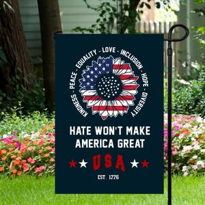 May include: A blue garden flag with a sunflower design featuring the American flag colors. The flag has the text "KINDNESS - PEACE - EQUALITY - LOVE - INCLUSION - HOPE - DIVERSITY" in a circle around the sunflower. The text "HATE WON'T MAKE AMERICA GREAT" is below the sunflower. The flag also has the text "★USA★ EST. 1776" at the bottom.