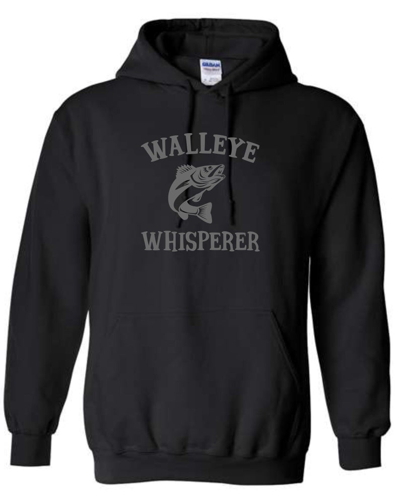 K&ouml;nnte beinhalten: Schwarzer Kapuzenpullover mit einem grauen Aufdruck eines Zanderfisches und dem Text "Walleye Whisperer".