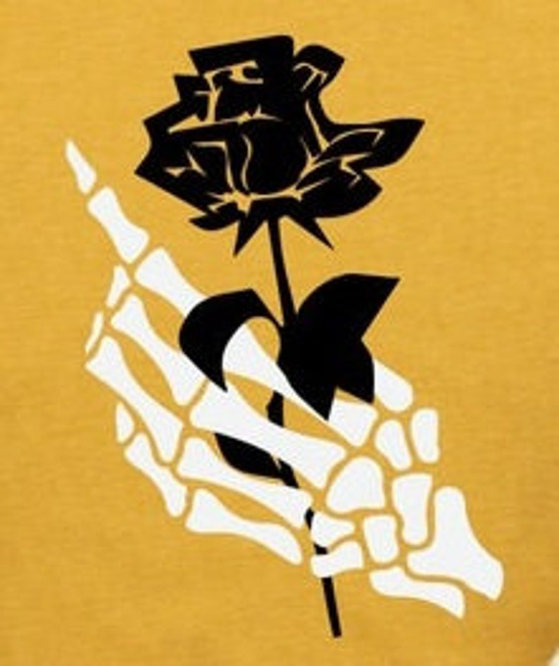 Peut inclure: Une rose noire tenue par une main squelettique blanche. La rose est au centre de l'image et la main est sur le c&ocirc;t&eacute; gauche de l'image.