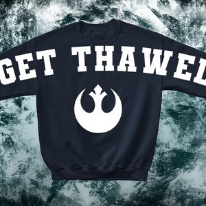 May include: A navy blue sweatshirt with the words "GET THAWED" in white block letters across the shoulders. A white emblem is centered on the chest. The sweatshirt has long sleeves.