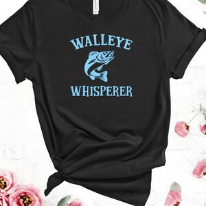 K&ouml;nnte beinhalten: Schwarzes T-Shirt mit einem blauen Walleye-Fisch-Motiv und dem Text "WALLEYE WHISPERER".