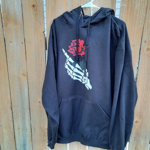 Peut inclure: Sweat-shirt &agrave; capuche noir avec un graphique de main squelettique blanche tenant une rose rouge.
