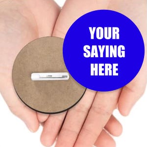 May include: A round button with a blue circle and the text "YOUR SAYING HERE" in white. The button is held in open hands, and has a pin on the back. The button is brown.