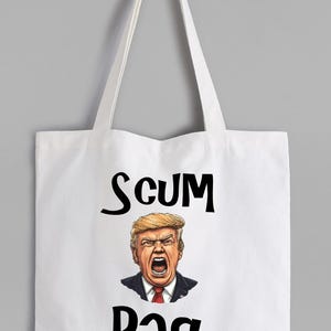 May include: White tote bag with black text that reads "SCUM BAG". The bag features a cartoon illustration of a man with blonde hair, an angry expression, and a red tie.