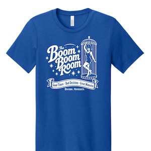 May include: A royal blue short-sleeve t-shirt featuring a white graphic print. The design includes the text 'The Boom Boom Room', a figure inside a birdcage, and a banner reading 'Good Times - Bad Decisions - Great Memories' with 'Biwabik, Minnesota'.